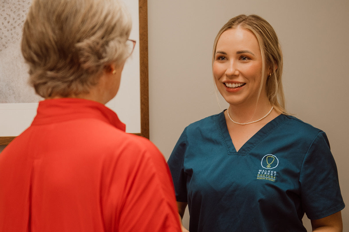 Woman in blue scrubs smiling at another person wearing a red jacket.