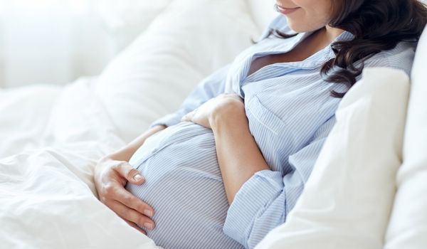 Pregnant woman in a light blue striped shirt holding her belly on a white couch.