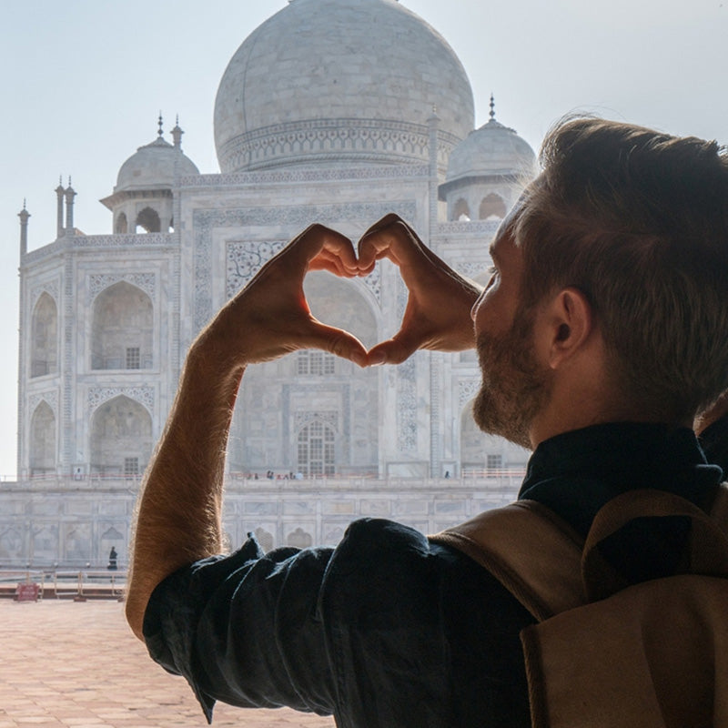 Person making a heart shape with their hands in front of the Taj Mahal.