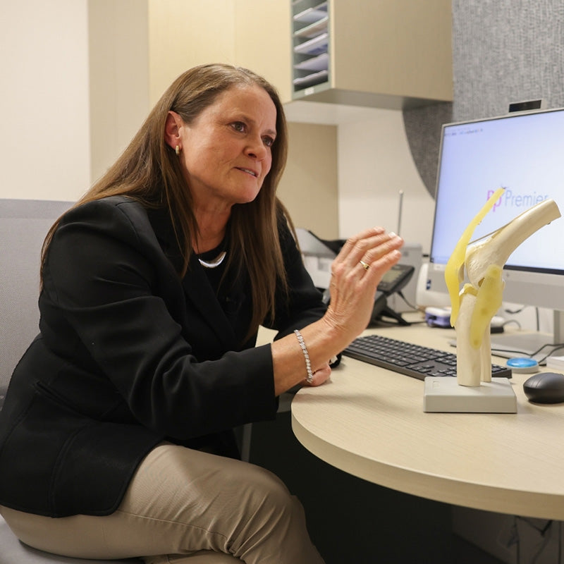 Dr Nerida McDonald sitting at a desk with a computer and anatomical model in an office setting